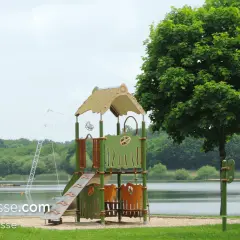 Aire de jeux près de l'étang de Buhel, avec un toboggan et un portique. Le logo WakePark Plessé est visible.