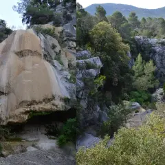 Cascade du Latay : formation rocheuse ocre et végétation luxuriante dans un paysage de garrigue.