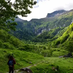 Une randonneuse explore le cirque de Cagateille, un paysage verdoyant de montagnes, de forêts et de cascades.