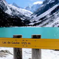 Panneau jaune indiquant "Lac de Gaube 1725 m" devant un lac turquoise et des montagnes enneigées.