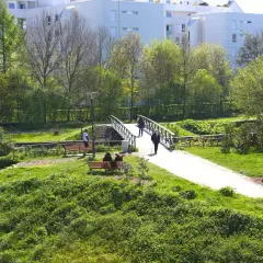 Promenade paisible aux prairies Saint-Martin à Rennes, avec un pont traversant un cours d'eau et des résidents profitant du soleil sur des bancs.