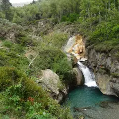 La cascade de l'Artigue dévale dans un bassin d'eau turquoise, entourée de roches et d'une végétation luxuriante.