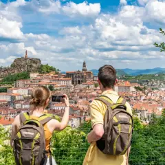 Couple avec sacs à dos admire la vue panoramique du Puy-en-Velay, capturant le moment pour immortaliser leur visite à pied.