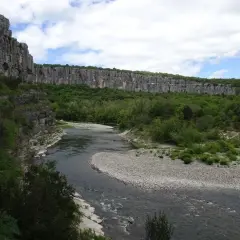 Rivière serpentant dans un cirque de falaises calcaires, le cirque de gens ruoms, bordé de verdure luxuriante.