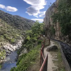 Sentier longeant un canal d'eau vive dans les gorges de la Guillera, avec une rivière en contrebas et des montagnes verdoyantes.