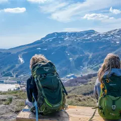 Deux randonneurs contemplent le paysage depuis le Puy de Chambourguet. Le lac scintille, les montagnes enneigées se dressent à l'horizon.