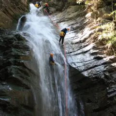 Descente en rappel le long de la cascade de Nyon. Des canyoneurs descendent une chute d'eau spectaculaire, entourés par la roche et la végétation luxuriante.