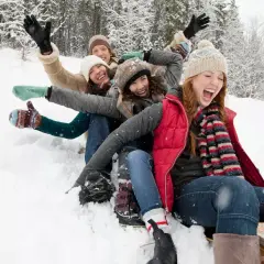 Des amis s'amusent en luge dans la neige, une scène joyeuse typique d'Annecy en décembre.