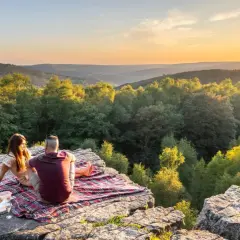 Un couple partage un pique-nique au coucher du soleil sur le roc la tour, surplombant une vallée boisée.