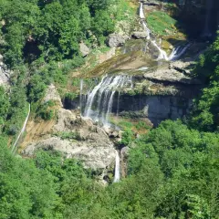 La cascade de la Charabotte dévale une falaise rocheuse, entourée d'une végétation luxuriante. L'eau forme de multiples bras sur les rochers.