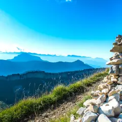 Un cairn de pierres marque le sommet, offrant une vue panoramique sur la grande sure et les montagnes bleutées à perte de vue sous un ciel clair.