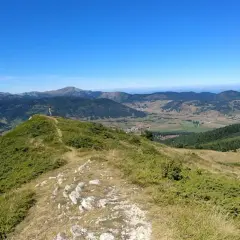 Vue panoramique depuis le col du Chioula, avec un randonneur contemplant les montagnes verdoyantes et le ciel bleu.