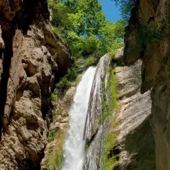 La chute de la druise, une cascade spectaculaire, dévale une falaise rocheuse verdoyante, entourée par la végétation luxuriante et le ciel bleu.