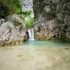 Cascade d'eau tombant dans un bassin turquoise au cœur de la gorge du Nan, entourée de falaises rocheuses et de végétation luxuriante.