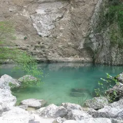 Le gouffre de la Fontaine de Vaucluse, une eau turquoise limpide émergeant d'une falaise rocheuse, entourée de végétation luxuriante et de rochers.