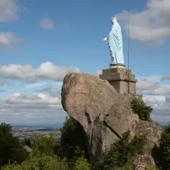 Statue de la Vierge sur la butte de Suin, veillant sur la vallée sous un ciel bleu parsemé de nuages.