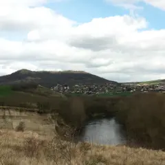 Vue panoramique d'une rivière sinueuse bordée d'arbres, avec une falaise de malmouche en contrebas et un village niché sur une colline verdoyante.