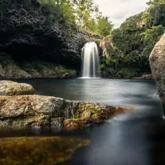 Magnifique cascade piscine naturelle en Ardèche, entourée de rochers et de végétation luxuriante. L'eau tombe en voile blanc dans le bassin sombre.