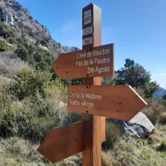 Panneau indicateur de randonnée : direction Cime de Baudon, Pas de la Piastre, Ste-Agnès, Col de la Madone et Gorbio village. Paysage montagneux.