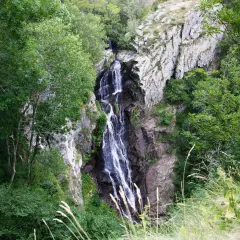 La cascade de Cubserviès dévale une falaise rocheuse, entourée d'une végétation luxuriante. L'eau blanche contraste avec le sombre des rochers.