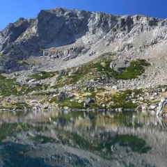 Reflets parfaits des montagnes rocheuses sur le lac de Bastani, sous un ciel bleu éclatant.