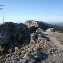 Vue panoramique depuis le pic des mouches, avec un anémomètre sur un rocher et un paysage de montagnes et de vallées sous un ciel bleu.