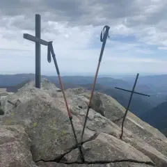 Sommet du pic des 3 Seigneurs. Deux croix et des bâtons de randonnée sur un rocher, avec une vue panoramique sur les montagnes.