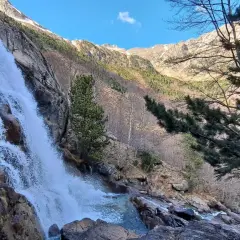 La cascade des Molières dévale une paroi rocheuse, entourée de pins et de montagnes enneigées sous un ciel bleu.