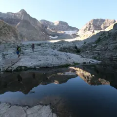 Randonneurs traversant un paysage rocheux près du lac du Portillon, avec des montagnes imposantes en arrière-plan.