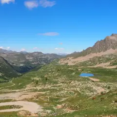 Vue panoramique du col de la Lombarde, avec des montagnes verdoyantes, des lacs bleus et un ciel clair.
