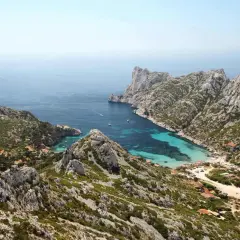 Vue aérienne de la calanque de Sormiou, un joyau bleu turquoise niché entre des falaises rocheuses. L'itinéraire pour y accéder est visible, serpentant à travers la végétation méditerranéenne.