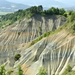 Le ravin de Corboeuf, un paysage spectaculaire aux strates colorées sculptées par l'érosion, dominé par une forêt verdoyante.