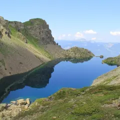 Le lac du Crozet, d'un bleu profond, reflète les montagnes escarpées et le ciel clair. Un paysage alpin paisible.