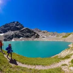 Randonneurs découvrant le magnifique lac de l'Eychauda, aux eaux turquoise vives, sous un ciel d'azur éclatant.