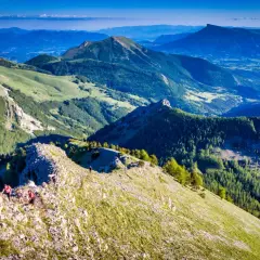 Randonneurs sur la crête rocheuse menant au pic de Gleize, avec des montagnes verdoyantes et un ciel bleu.