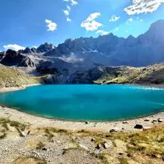 Magnifique lac Saint-Anne aux eaux turquoise, entouré de montagnes rocheuses et de pentes herbeuses sous un ciel bleu éclatant.