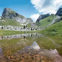 Le lac de Darbon, paisible, reflète les montagnes verdoyantes et rocheuses sous un ciel bleu et nuageux.