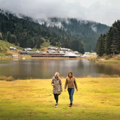Deux amies profitent d'une promenade au bord du lac de Payolle, entouré de forêts et de montagnes brumeuses.