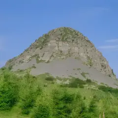 Le rocher de Sampzon, imposant et rocheux, se dresse sous un ciel bleu. Des arbres verts l'entourent.
