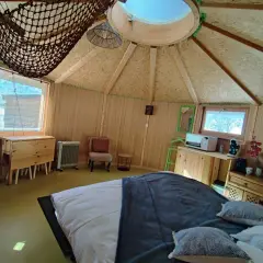Intérieur douillet d'une yourte au col du Festre, avec un lit confortable, une kitchenette et une vue sur la nature.