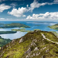 Vue panoramique du lac du Connemara, un lieu d'une beauté sauvage avec des montagnes verdoyantes et des eaux bleues scintillantes sous un ciel nuageux.