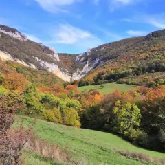 Vallée automnale aux couleurs vives, menant à la cascade de Chaudeyrolles. Le ciel bleu contraste avec les falaises et les arbres aux teintes orangées et vertes.