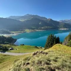 Vue panoramique du lac de la Gittaz aux eaux turquoise, entouré de montagnes verdoyantes et d'une route sinueuse.