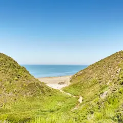 Vue sur la mer à travers la vallée du Lude, bordée de collines verdoyantes et d'une plage de sable.