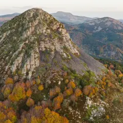 Vue aérienne du Mont Gerbier de Jonc en automne, ses pentes rocheuses et ses forêts aux couleurs flamboyantes. Une carte visuelle de ce paysage volcanique.