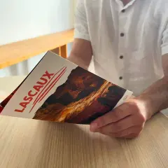 Un homme lit un dépliant sur la grotte de Lascaux, planifiant son itinéraire pour découvrir les peintures préhistoriques.