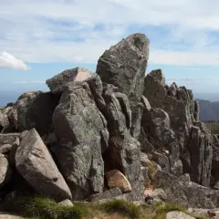 Rochers escarpés au sommet de la Punta di a vacca morta, avec des montagnes en arrière-plan sous un ciel bleu et nuageux.