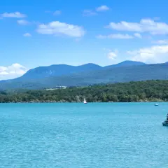 Le lac de Montbel, aux eaux turquoise, accueille un voilier et un petit bateau de pêche sous un ciel bleu parsemé de nuages.
