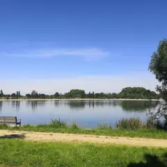 Un banc invite à la contemplation du lac de la Ramée sous un ciel bleu.