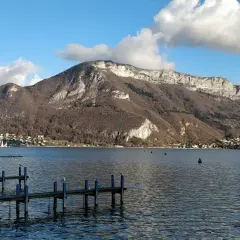 Vue de la webcam du lac d'Annecy, avec un ponton en bois et des montagnes majestueuses en arrière-plan.